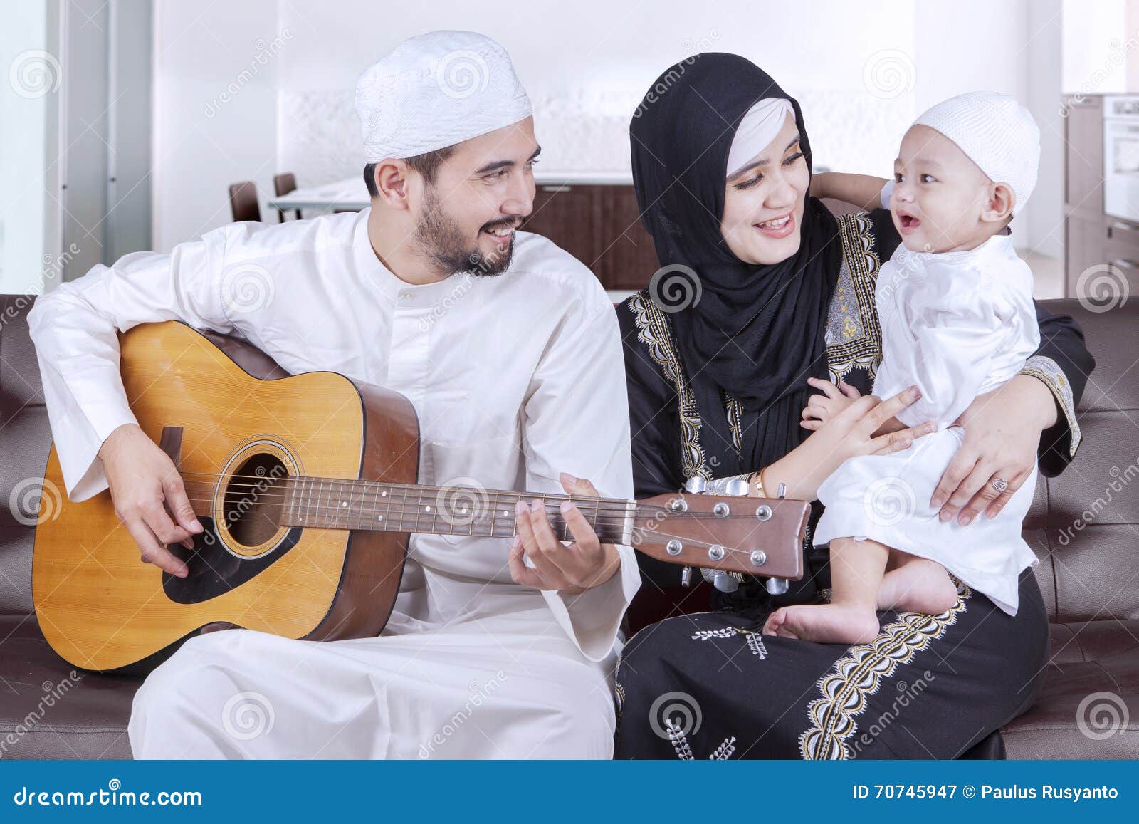 Joyful middle eastern family playing guitar. Image of joyful Arabian family having fun together while playing guitar on the sofa at home