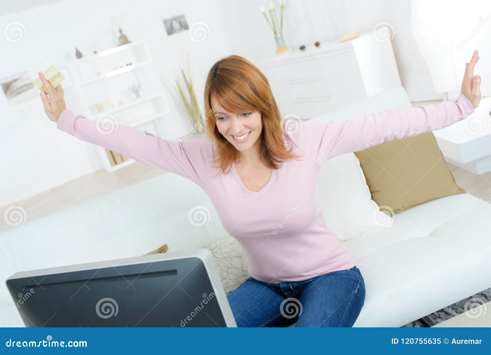 joyous woman holding bankcard and looking at computer screen