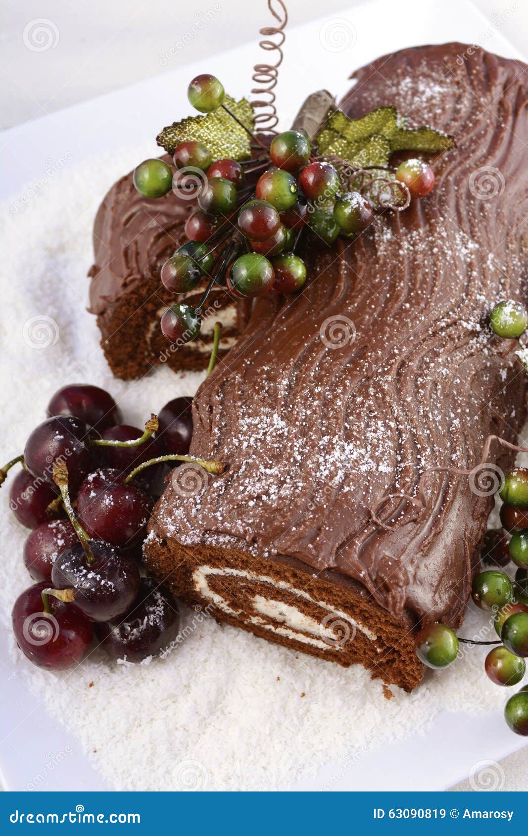 Jul Yule Log Cake. Jul Yule Log, Buche de Noel, chokladkaka med filialen, nya körsbär och festliga bärgarneringar på ett vitt portionuppläggningsfat som är över huvudet