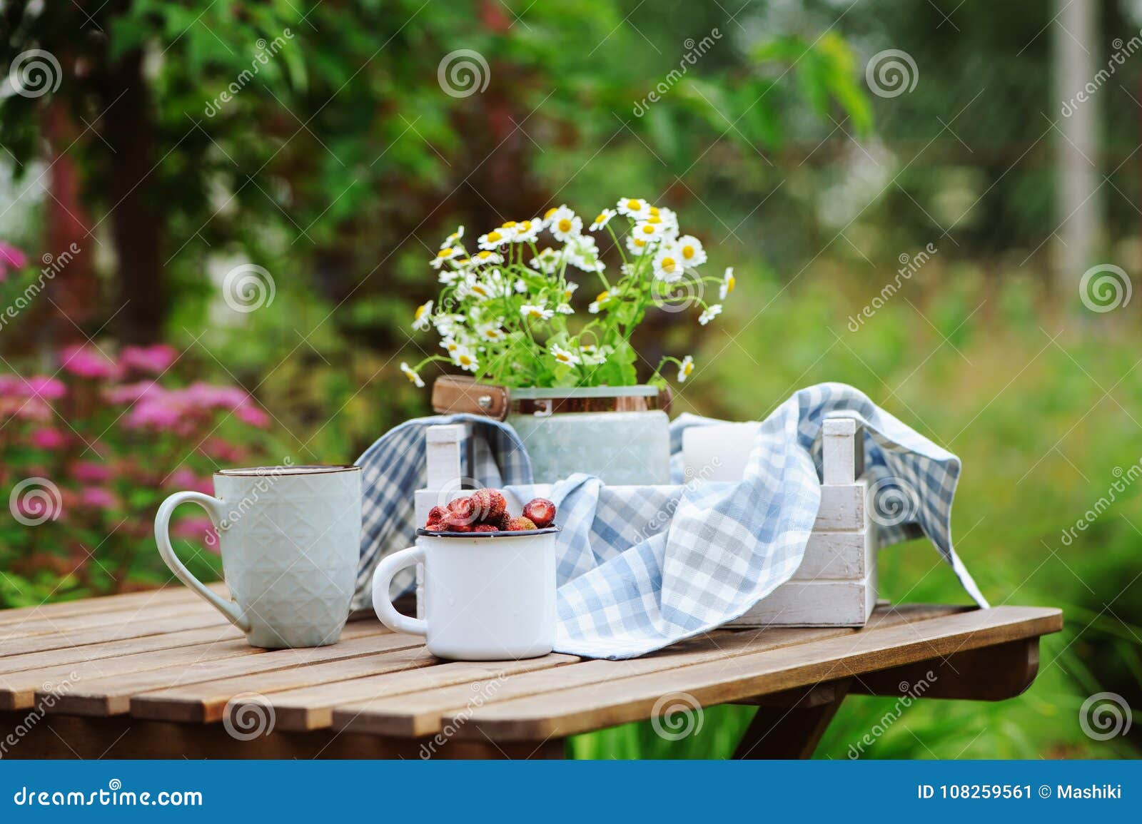 june or july garden scene with fresh picked organic wild strawberry and chamomile flowers on wooden table outdoor