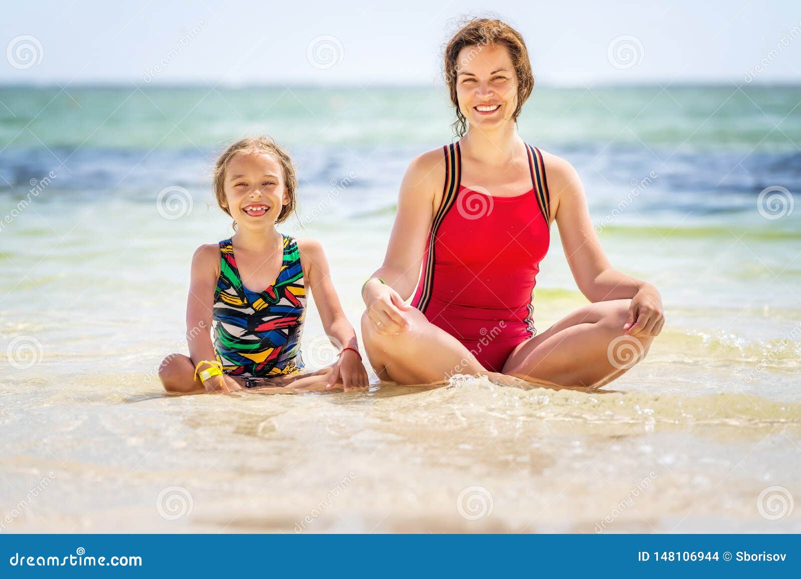Junge Mutter und kleine Tochter, die auf dem Strand in der Dominikanischen Republik sitzt