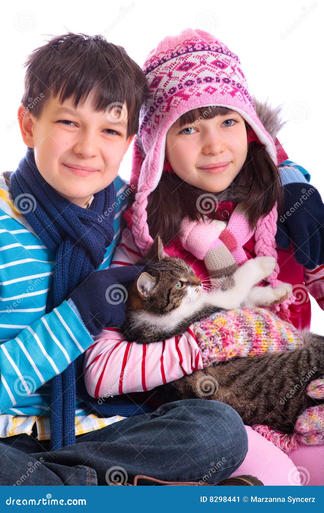 Jungen- und Mädchenholdingkatze. Eine Studioansicht eines jungen tragenden Winterhutes des Jungen und des Mädchens, des Schals und der Handschuhe, eine braune Katze anhalten. Weißer Hintergrund.