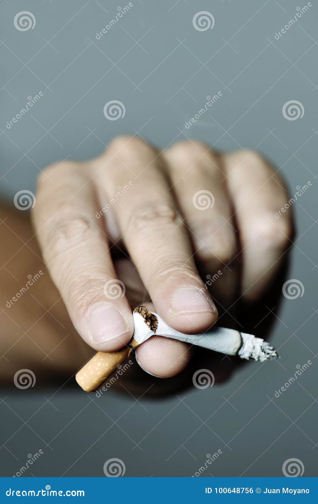 Junger Mann, der das Rauchen beendigt. Nahaufnahme der Hand eines jungen kaukasischen Mannes, der eine beleuchtete Zigarette mit seinen Fingern bricht