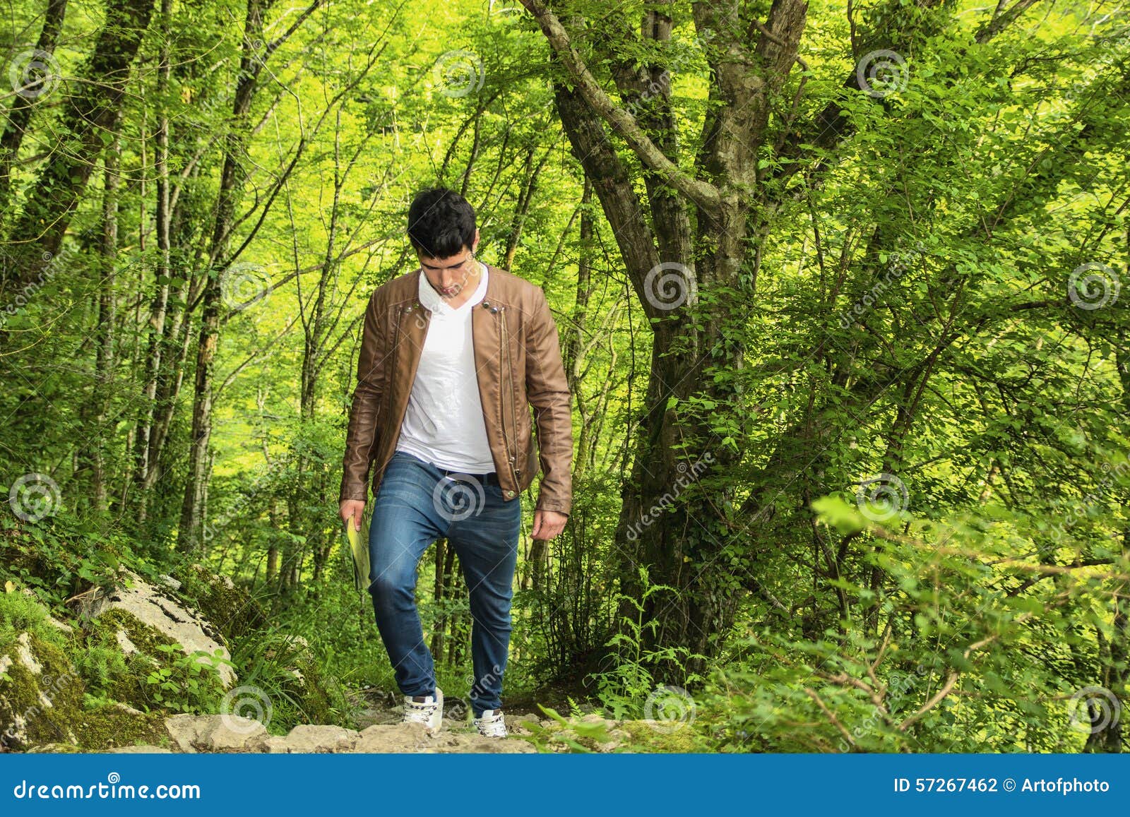 Junger Mann, der in der üppigen grünen Gebirgslandschaft wandert. Hübscher junger Mann, der in der üppigen grünen Gebirgslandschaft, gehend herauf den Hügel wandert und unten schauen