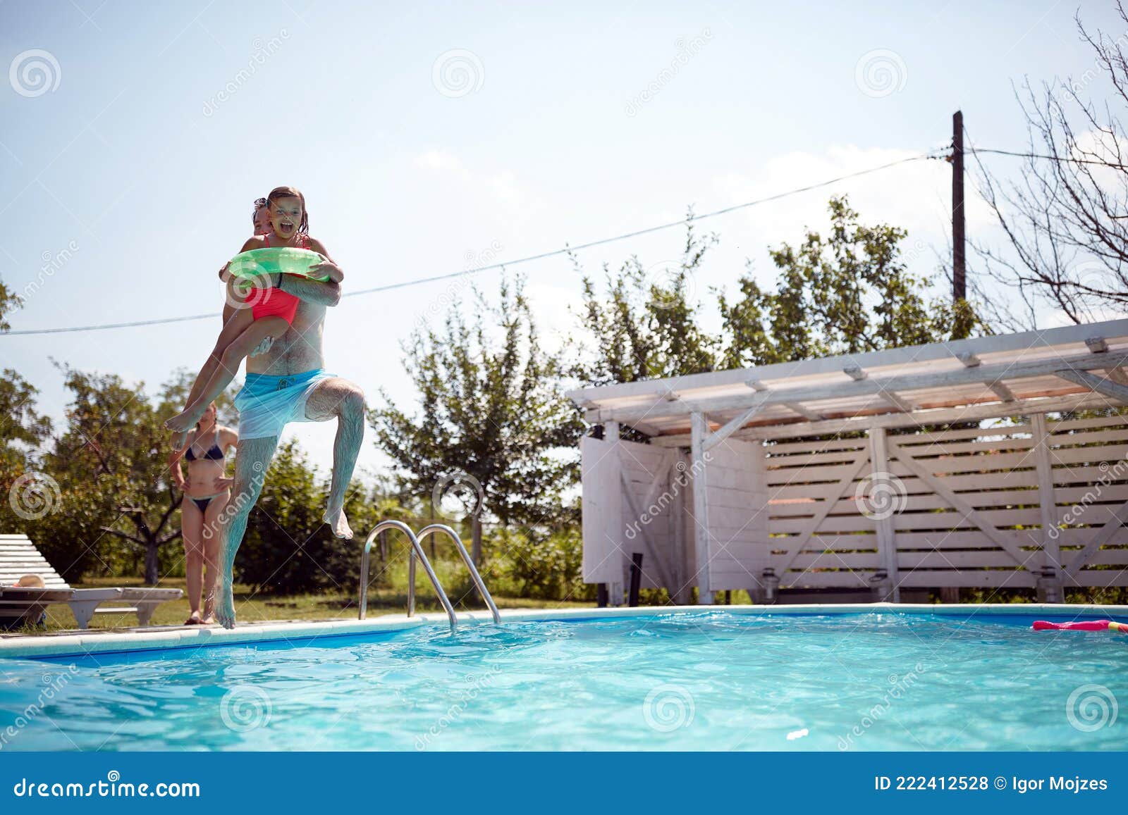 Junger Vater springt in ein Schwimmbad mit seiner Tochter in den Armen