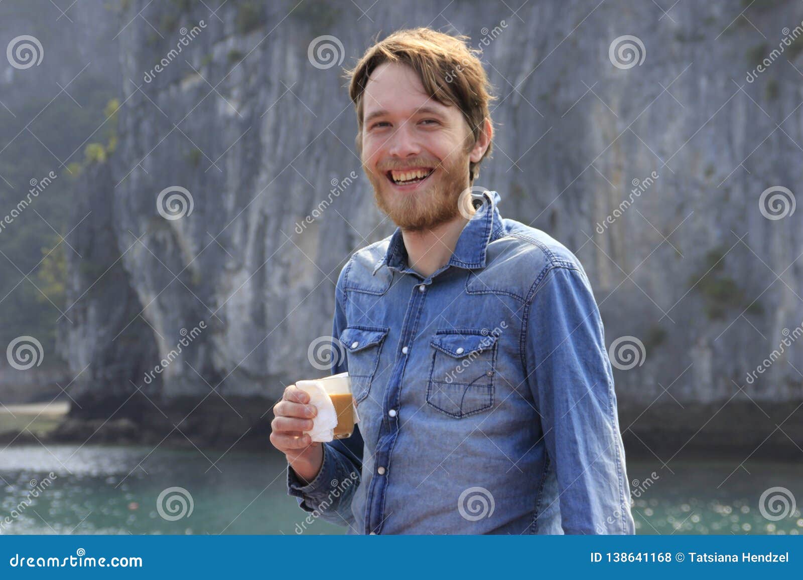 Junger Weisser Attraktiver Blonder Mann Mit Einem Bart In Einem Blauen Denimhemd Defiantly Lachend Mit Einem Glas Kaffee Auf Dem H Stockfoto Bild Von Blauen Blonder