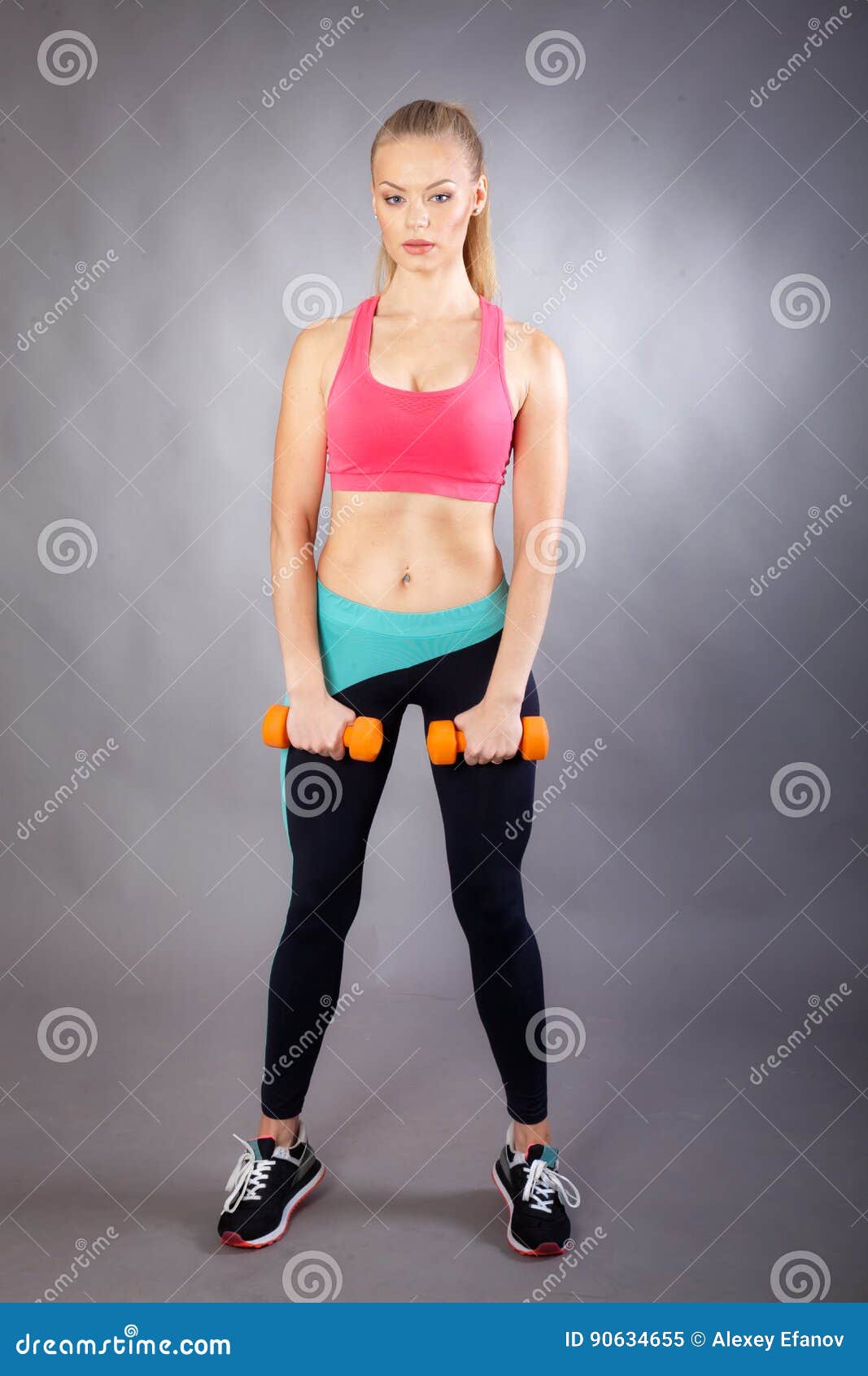 Junges Sportmädchen mit Dummköpfen. Porträt des jungen Sportmädchens mit Dummköpfen auf grauem Hintergrund