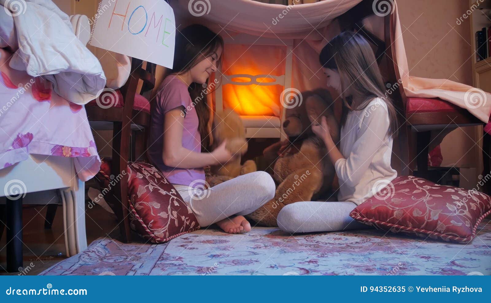 4K video of two smiling girls playing with teddy bear in their self-made house at living room in night