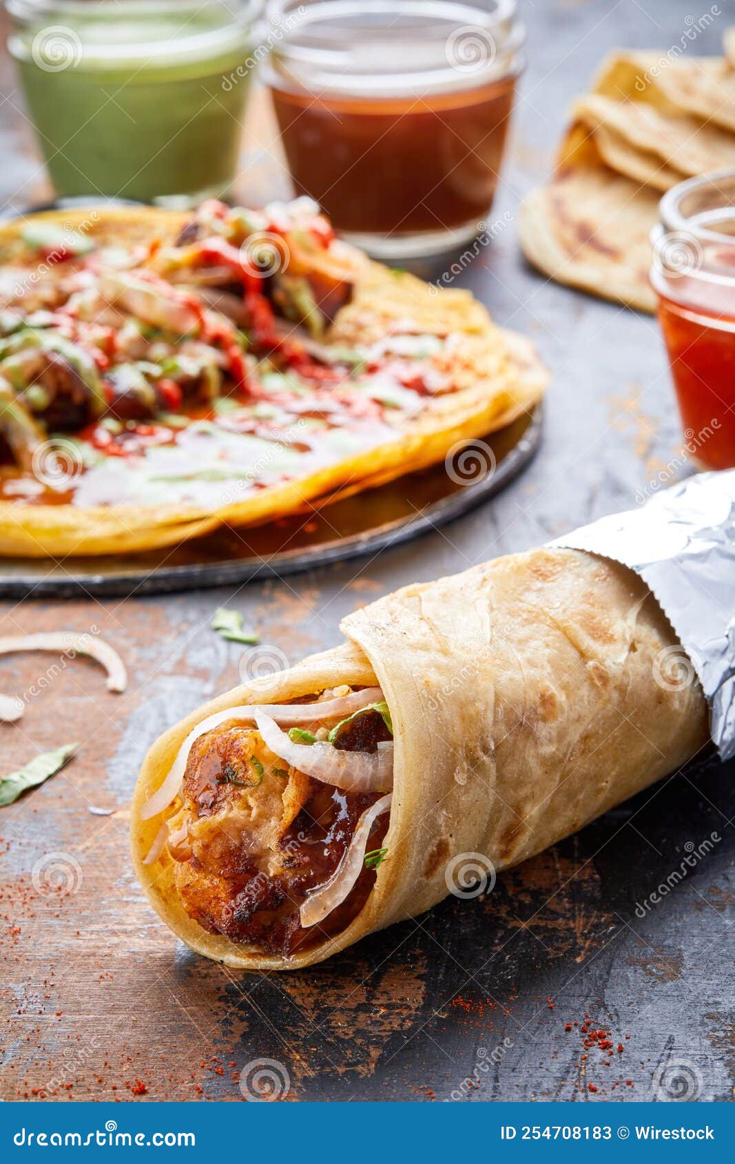 Kati Roll with Meat on a Table Against an Open Roll and Sauces in the