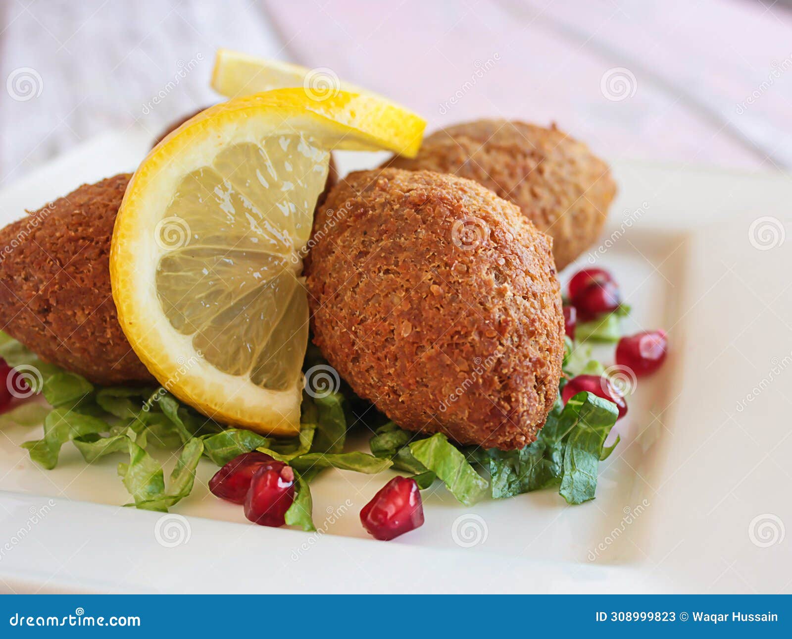 kebbah, kibbeh, kibbe or kubbeh with lemon slice and pomegranate seeds closeup served in dish  on table side view of
