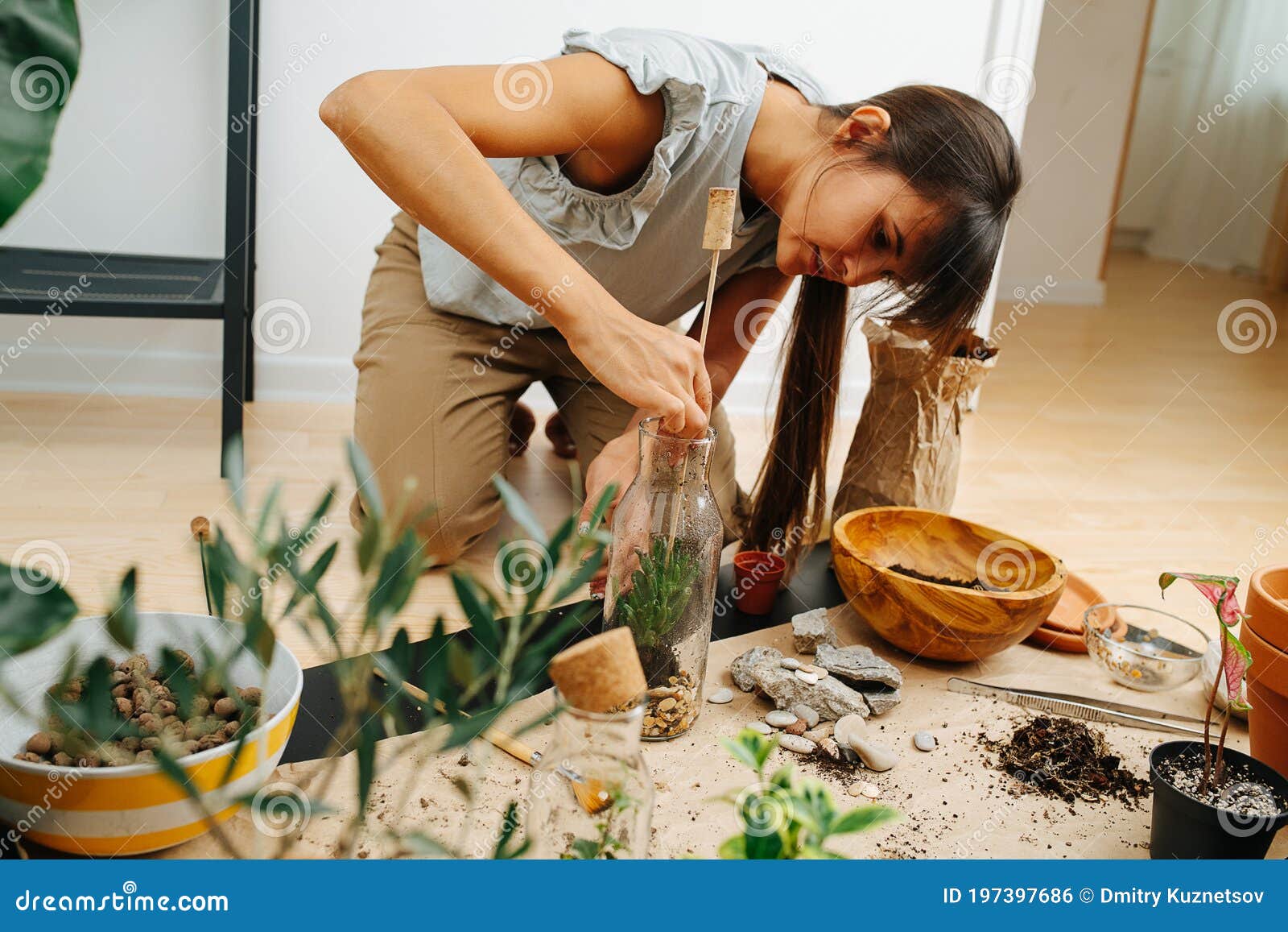 keen woman in living room planting inside glass bottle, using stick
