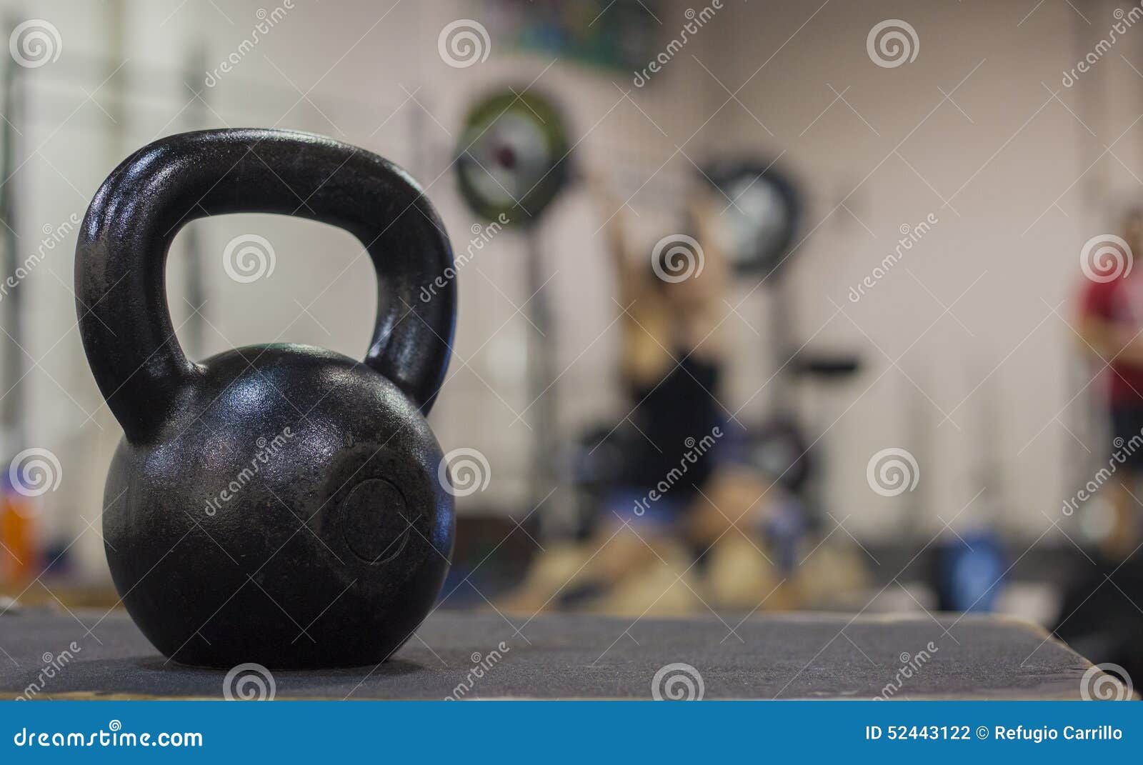 a cast iron kettle bell with a young women weight lifting in the background