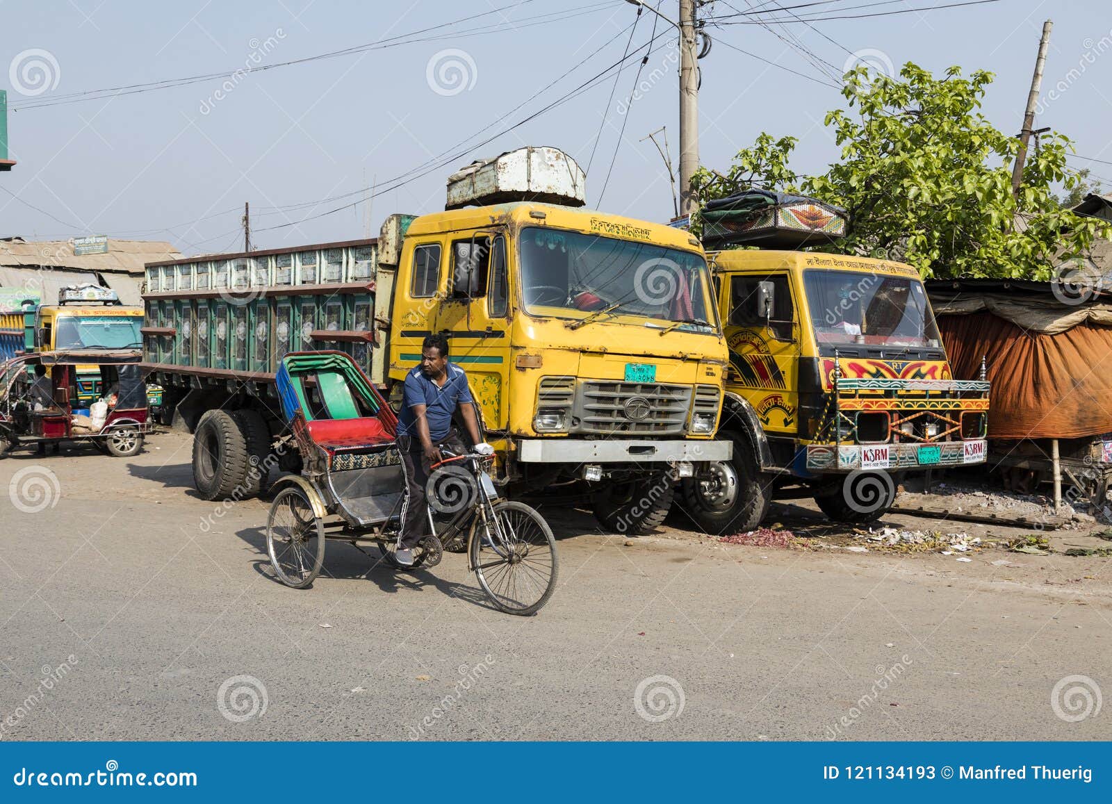Khulna, Bangladesch, am 28. Februar 2017: Trishaw-Fahrer-Antriebe in Khulna. Khulna, Bangladesch, am 28. Februar 2017: Trishaw-Fahrer fährt in Khulna vor einem LKW in der Straße