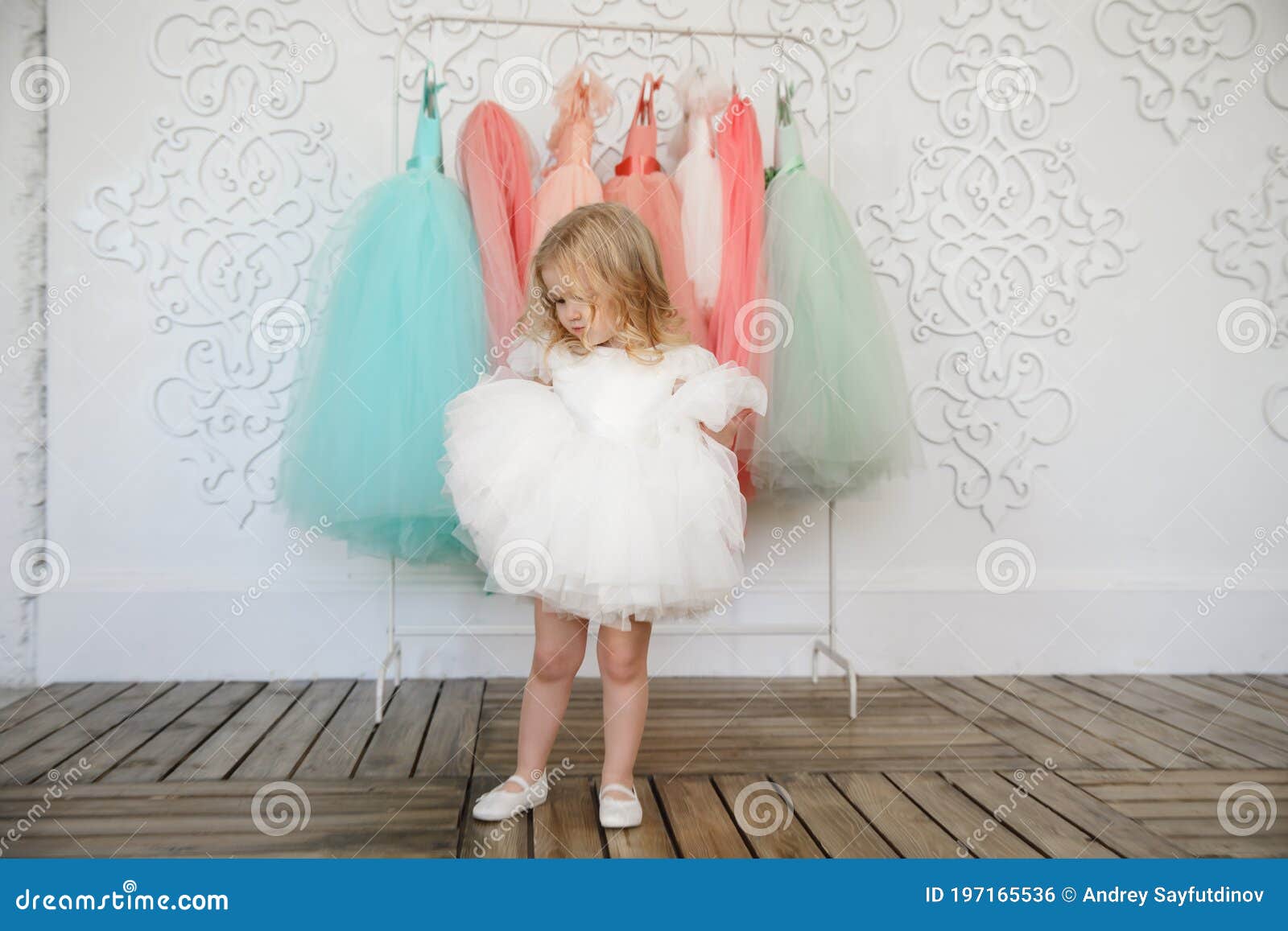 kid girl in dress near hanger with festive clothes