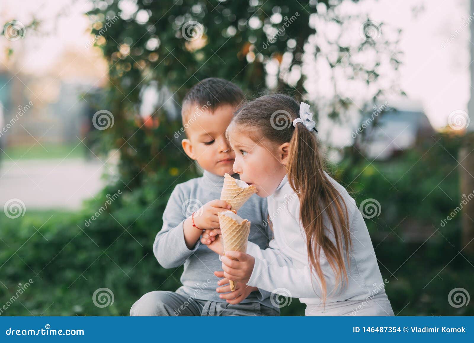 Kids Boy and girl eating ice cream outdoors on grass and trees background very sweet