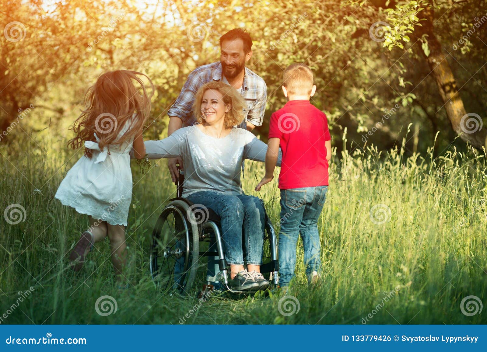 Kinderen aan hun gehandicapte moeder in het park in werking dat worden gesteld dat. Glimlachende Vrouw in Rolstoel en Man die zich achter Haar die Glimlachen bij Kinderenwho bevinden aan hen in werking worden gesteld Gehandicapte Moederspelen met Haar Jonge geitjes in het Park