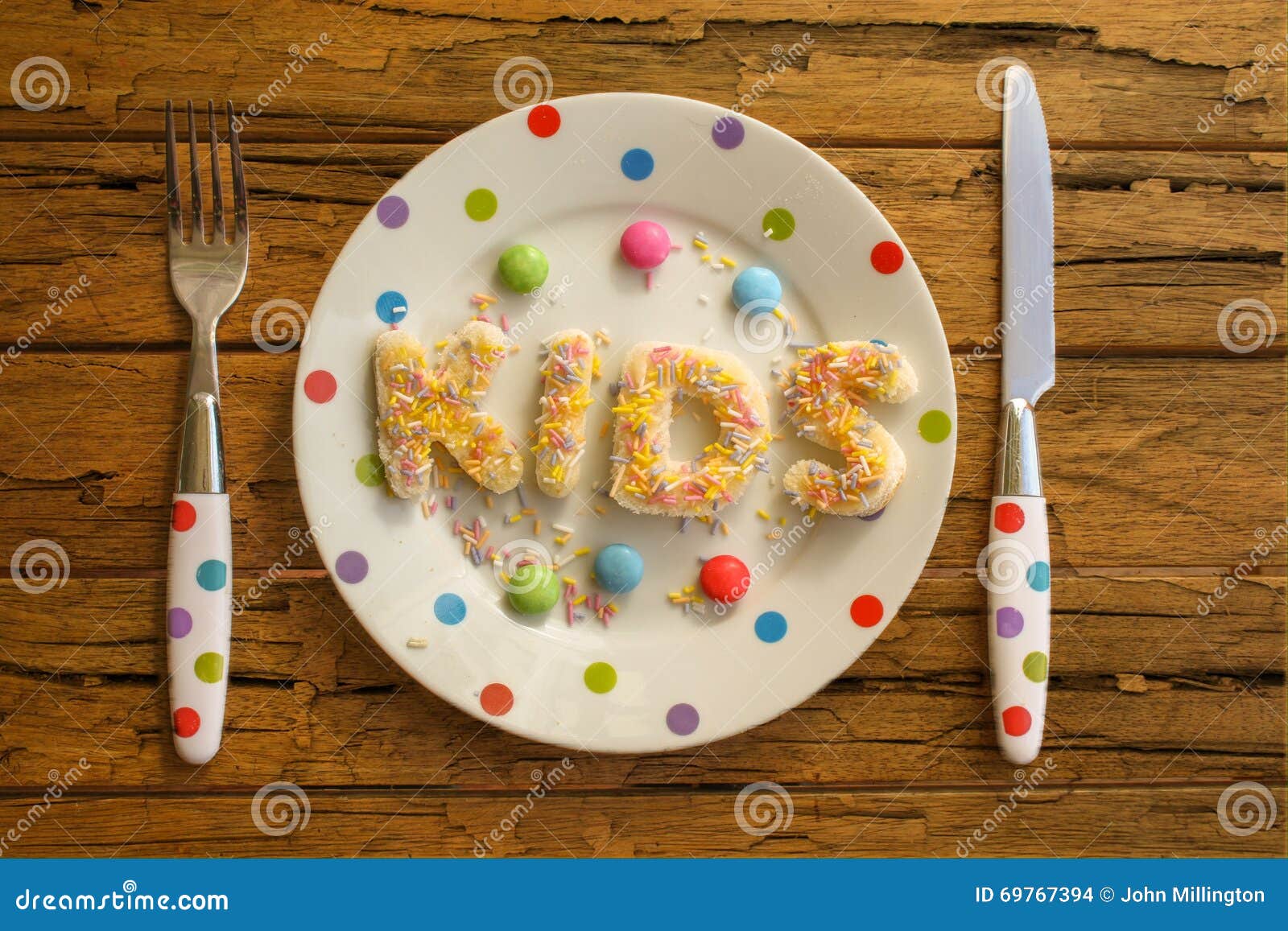Kinderpartei-Lebensmittel. Das Wort KINDER geschrieben in Kuchen auf eine beschmutzte Platte und ein Tafelsilber auf einen rauen Holztisch