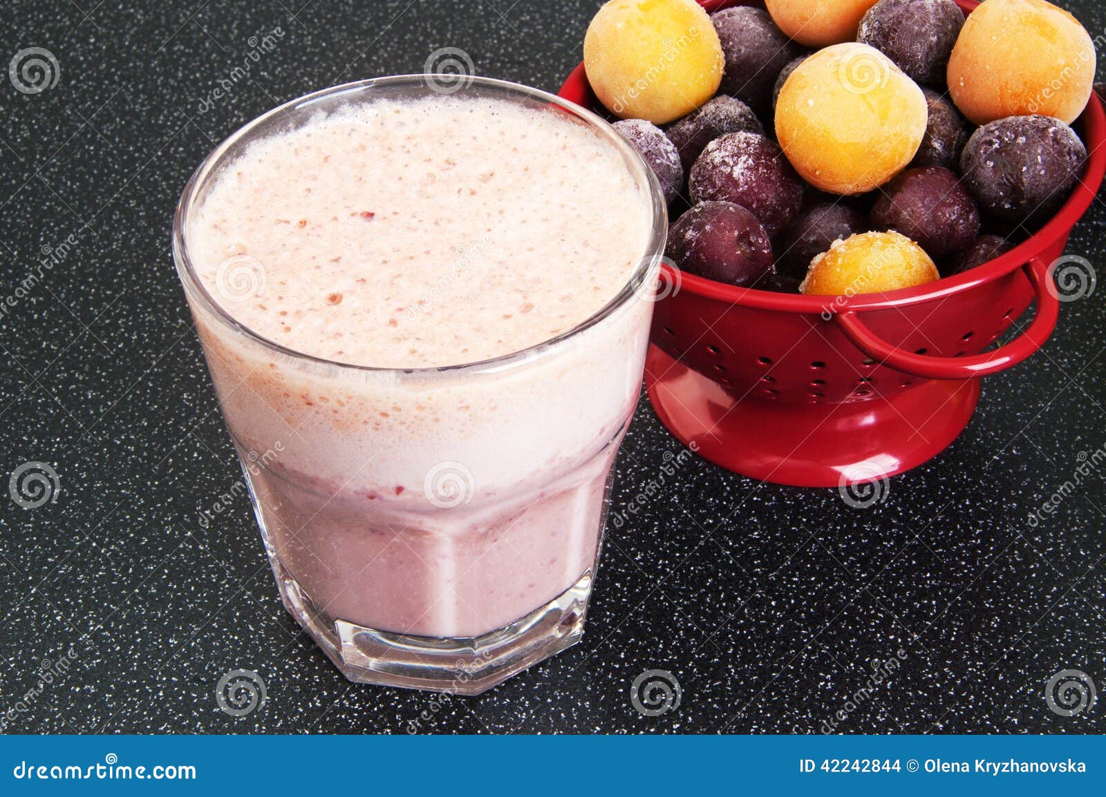 Kirschmilchshake in einer Glasschale und in einem roten Sieb mit gefrorenen Kirschen und Kirschepflaume auf einem dunklen Hintergrund