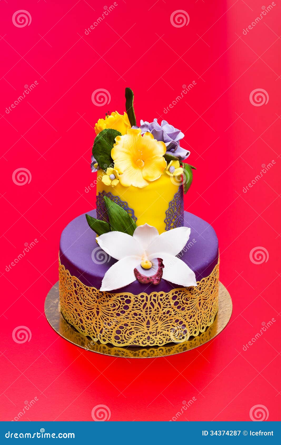 Kleurrijke die cake met suikergoedbloemen en kant wordt verfraaid. Kleurrijke purper-gele die cake met eetbaar suikergoedbloemen en kant wordt verfraaid