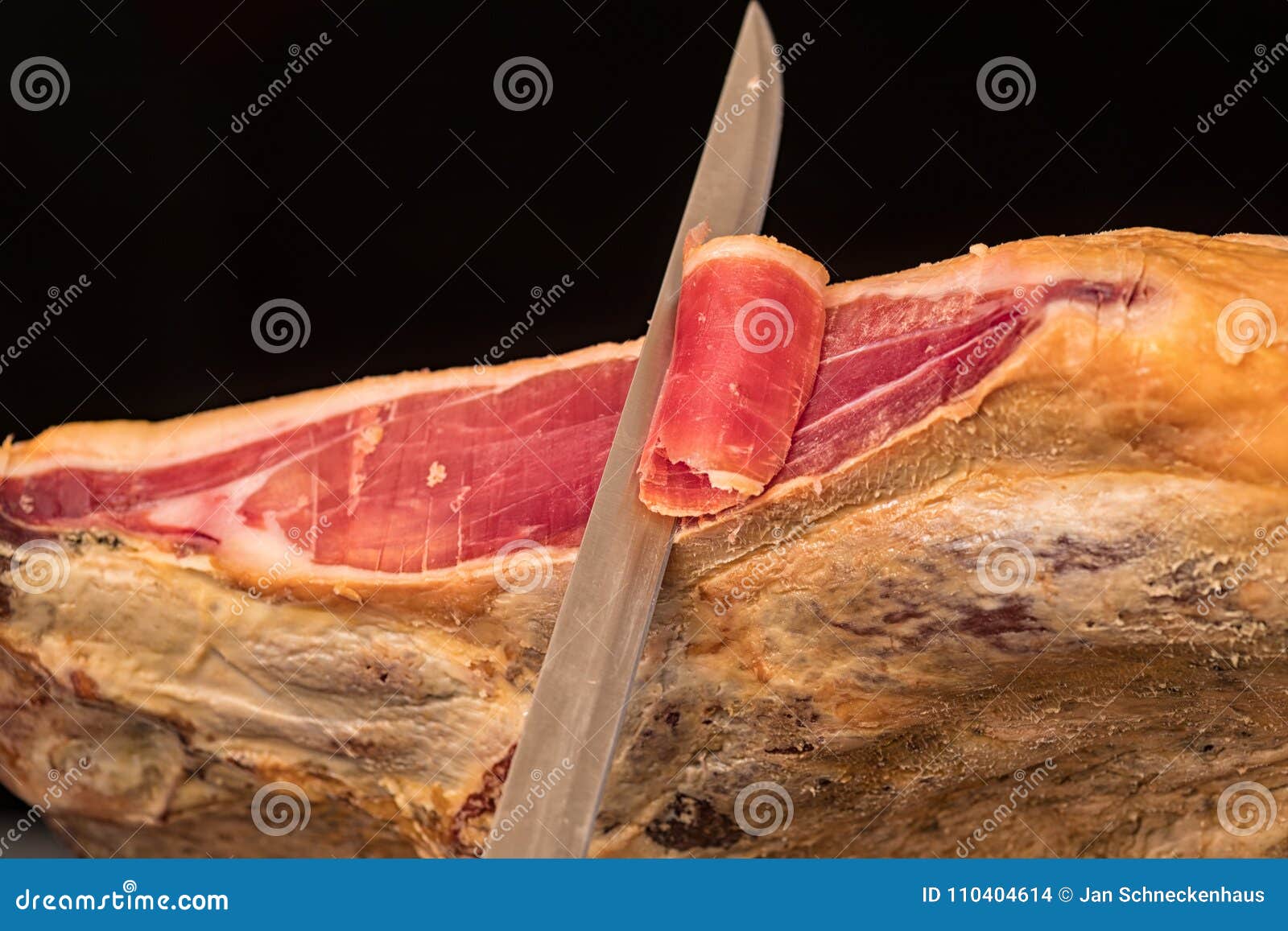 a knife cutting a spanish serrano ham