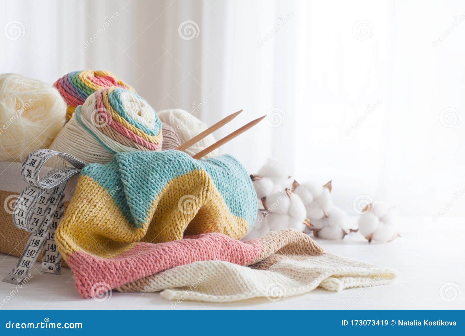 knitting wool and knitting needles in pastel colors on white background. cotton bolls. copy space