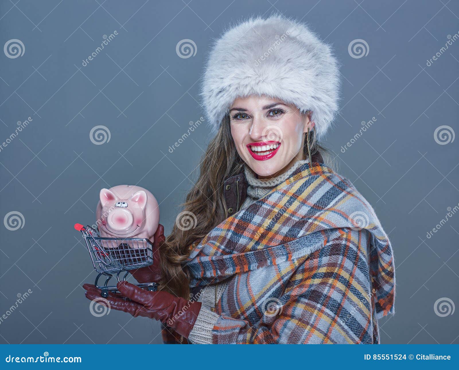 Kobieta odizolowywająca na zimnym błękitnym mienie zakupy tramwaju z prosiątkiem. Zim rzeczy Portret szczęśliwa młoda kobieta w futerkowym kapeluszu odizolowywającym na zimnym błękitnym mienie zakupy tramwaju z prosiątko bankiem