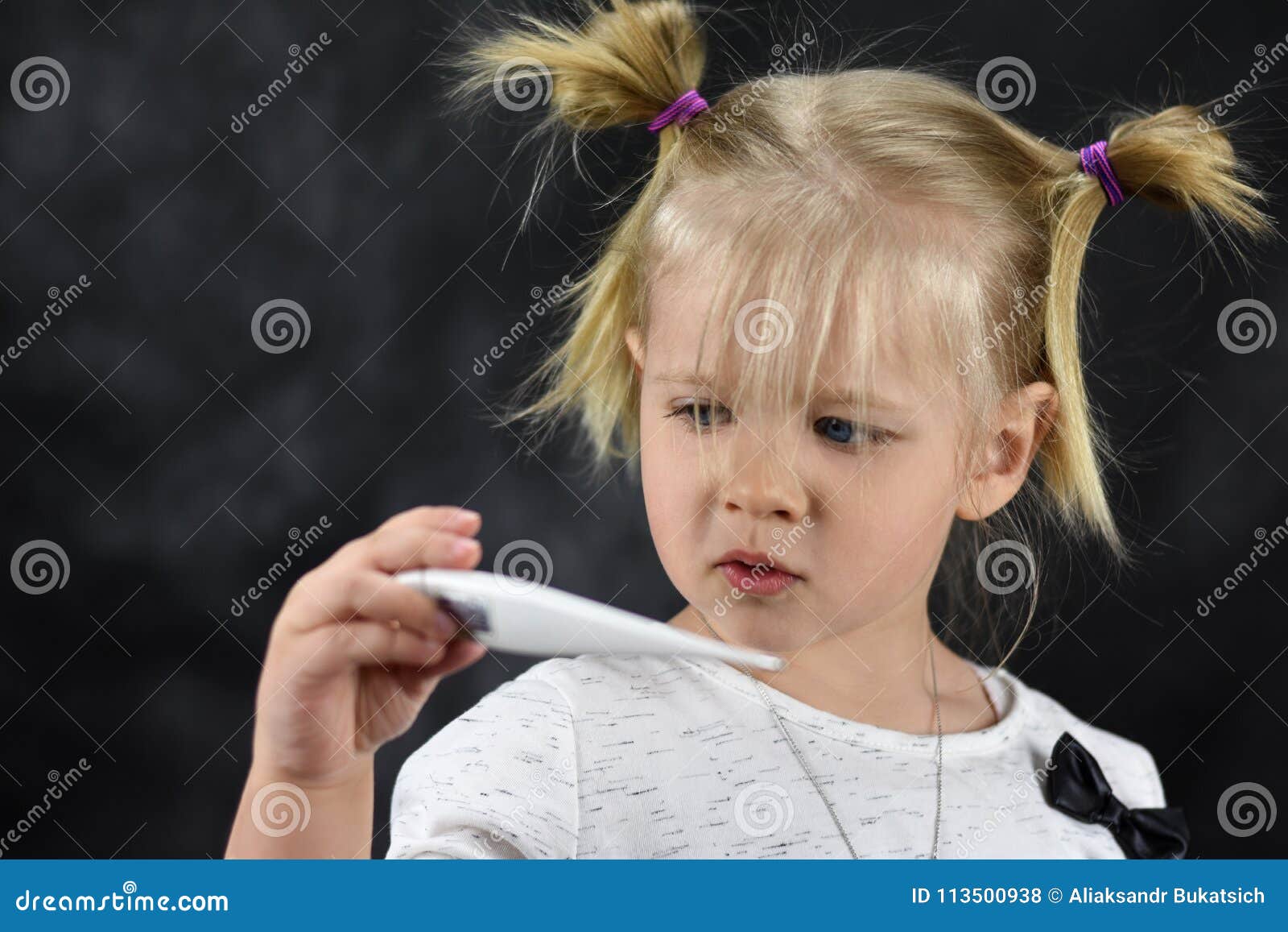 Krankes Mädchenkind betrachtet den Thermometer in der Hand. Kranker Mädchenkinderblick auf den Thermometer in der Hand