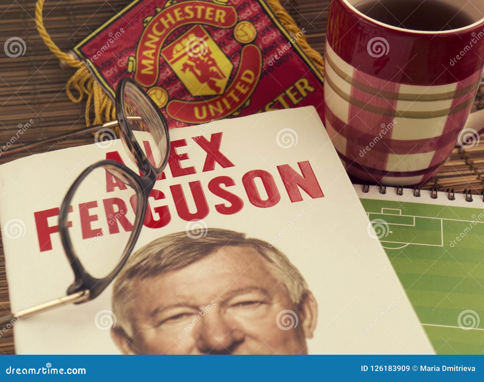 reading autobiography book by alex ferguson, a football coach. glasses, sports pennant