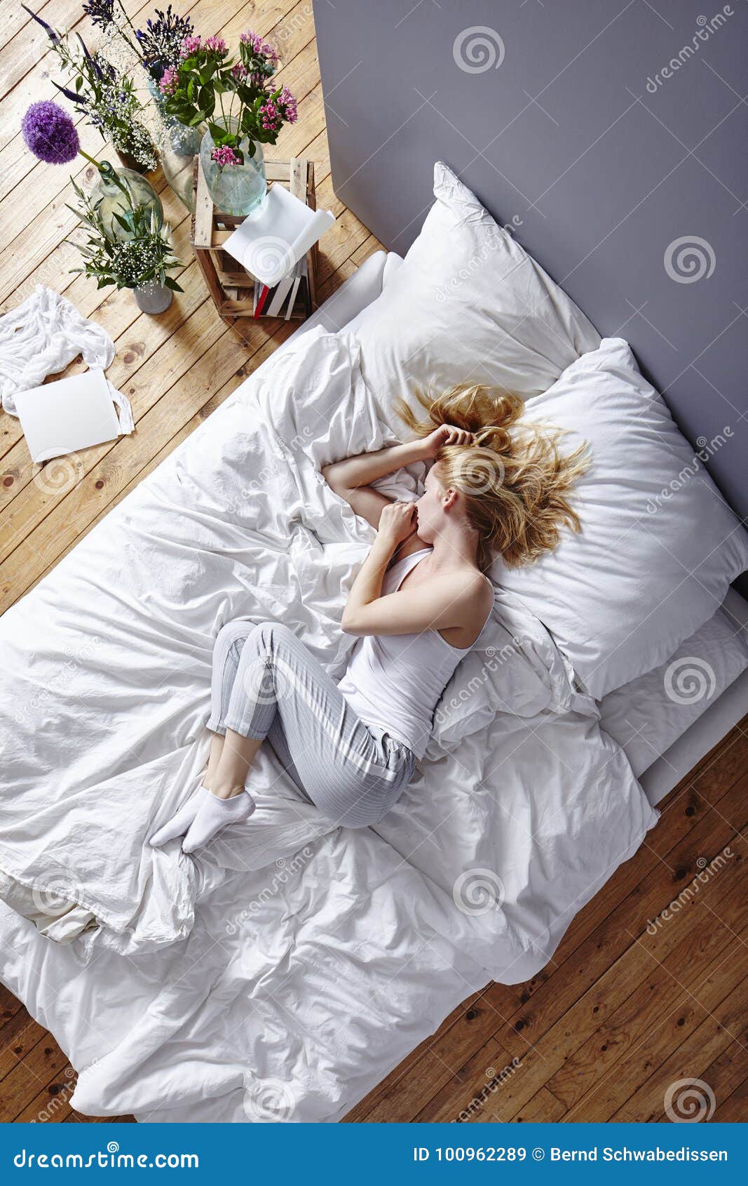 Krulla upp i säng. Ung kvinna som krullar sig upp i vitt landskap för lovande person för sängmorgonatmosfär