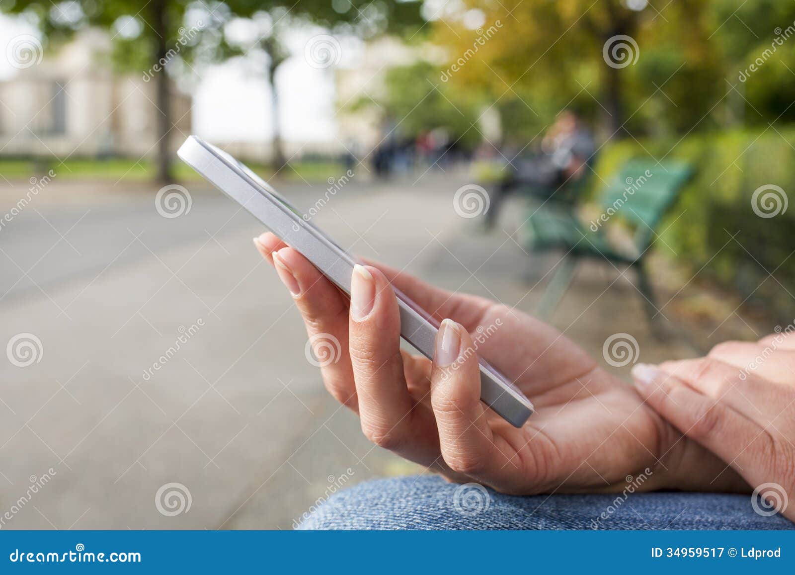 Kvinna med en mobiltelefon som sitter i en parkera på en bänk som läser a. Tar av planen kvinnliga mobiltelefonträd för närbild utomhus- meddelandesmsmejl