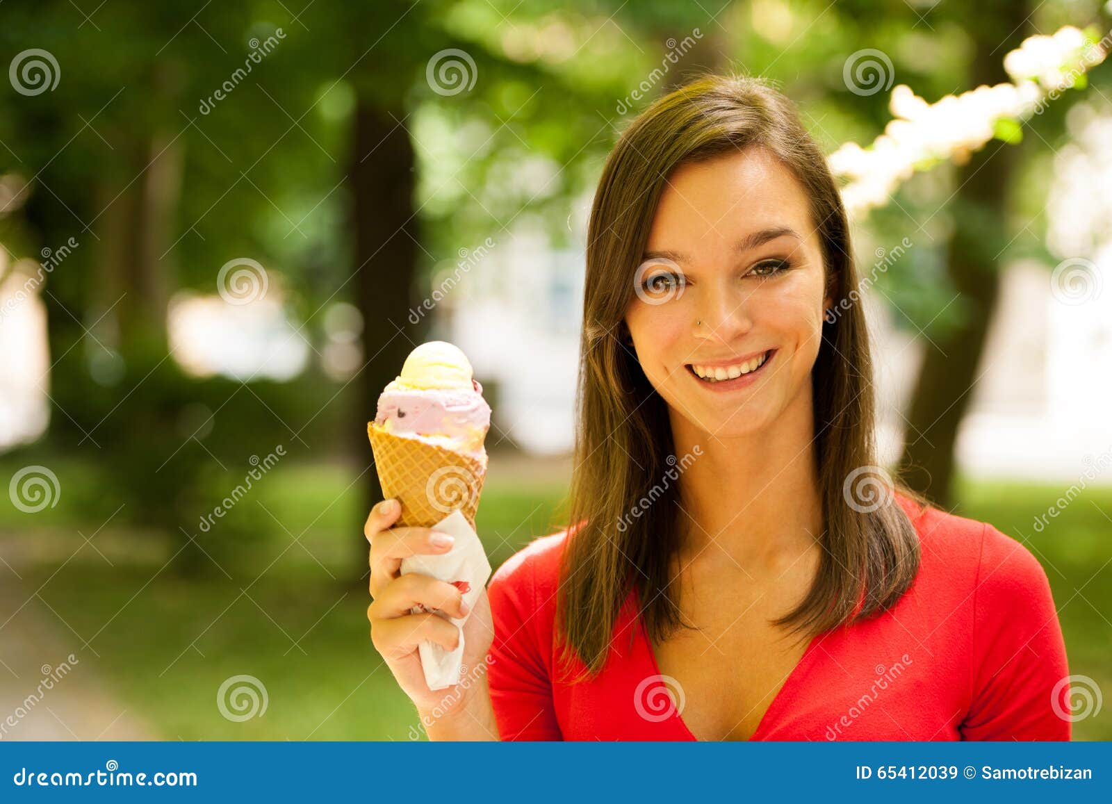 Kvinnan äter utomhus- söt glass parkerar in. Kvinnan i röd skjorta äter utomhus- stor smaklig söt glass parkerar in