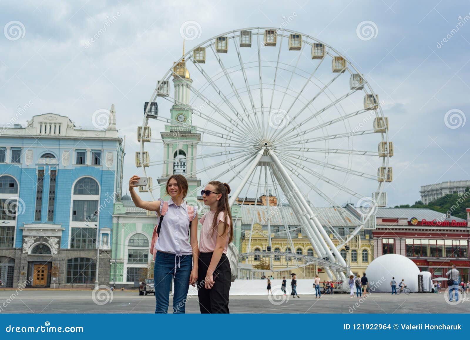 Kyiv UA, 19-07-2018 Европейский город, колесо ferris развлечений на квадрате Туристы маленьких девочек сфотографированы в backgro. Kyiv UA, 19-07-2018 Европейский город, колесо ferris развлечений на квадрате Туристы маленьких девочек сфотографированы на заднем плане колеса Ferris