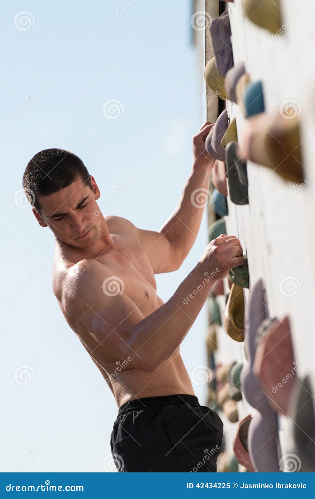 Kämpfen, zum des Griffs auf Kletterwand zu erreichen. Junger Mann klettert oben eine Freien-Felsen-Wand - er wird offenbar bestimmt, um sie zur Spitze zu machen