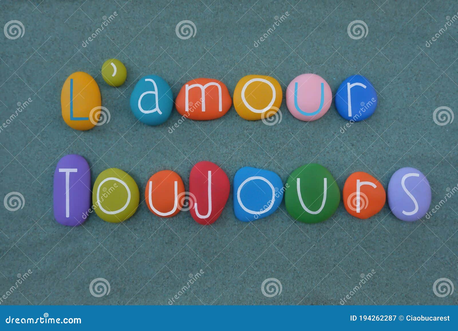 l`amour toujours, french phrase meaning love always composed with handmade multicolored stone letters over green sand