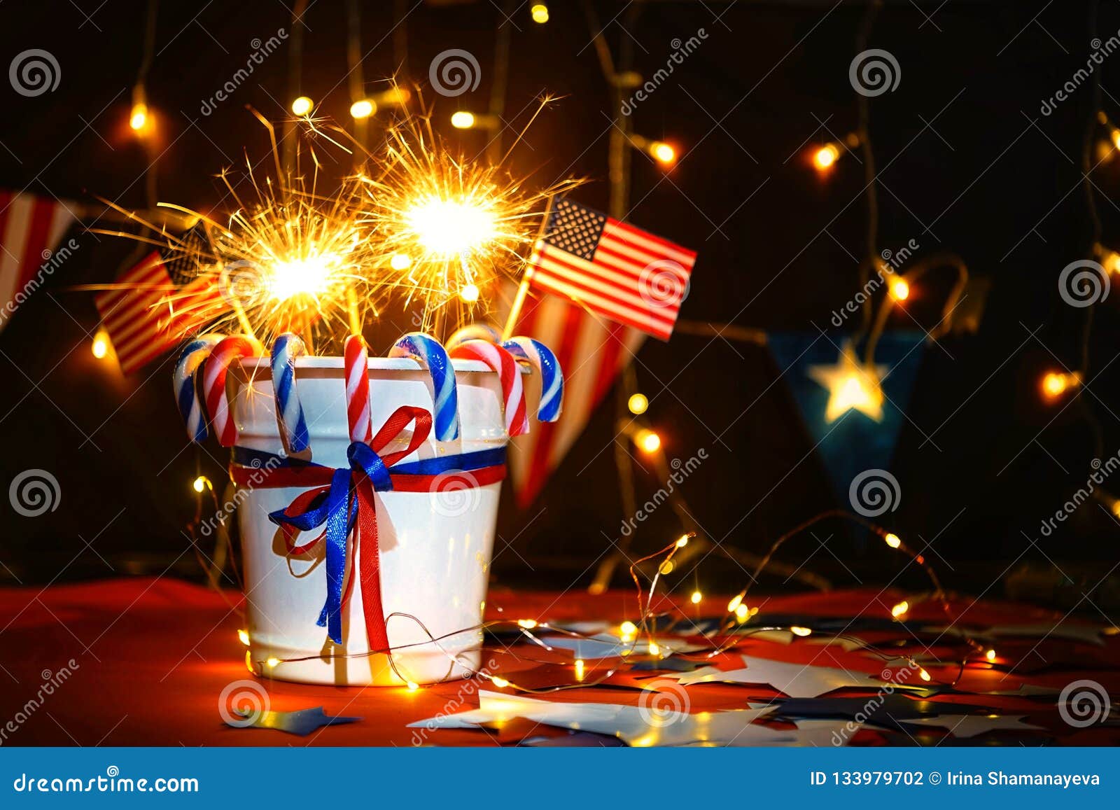 L'esposizione dei fuochi d'artificio celebra la festa dell'indipendenza della nazione degli Stati Uniti d'America sul quarto di luglio con noi bandiera, le stelle filante, caramella, sui precedenti rossi e sui precedenti della ghirlanda e del bokeh di Natale, con le stelle, la conclusione della celebrazione di libertà