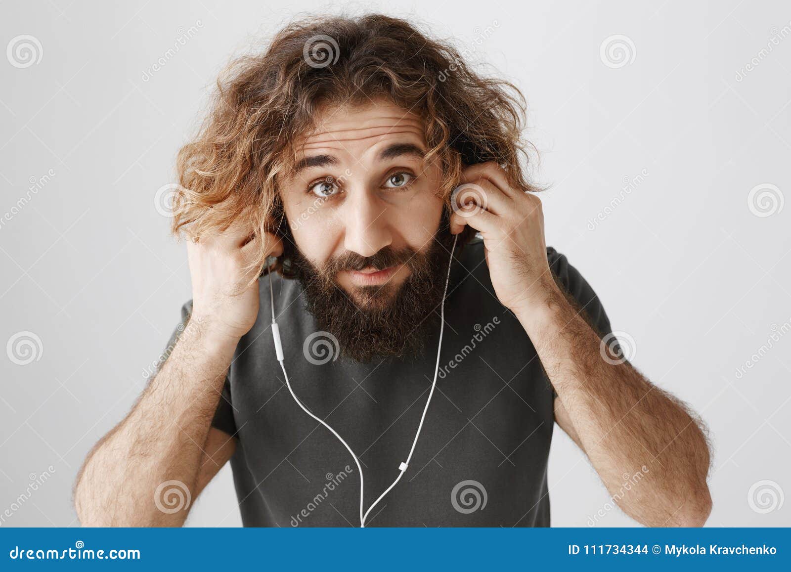 L'homme met sur des écouteurs pour aller pulser Le studio a tiré du type oriental aux cheveux bouclés beau avec la musique de écoute de barbe dans des écouteurs, regardant de dessous le front, n'ayant aucun indice quelle amie dit Concept de technologie