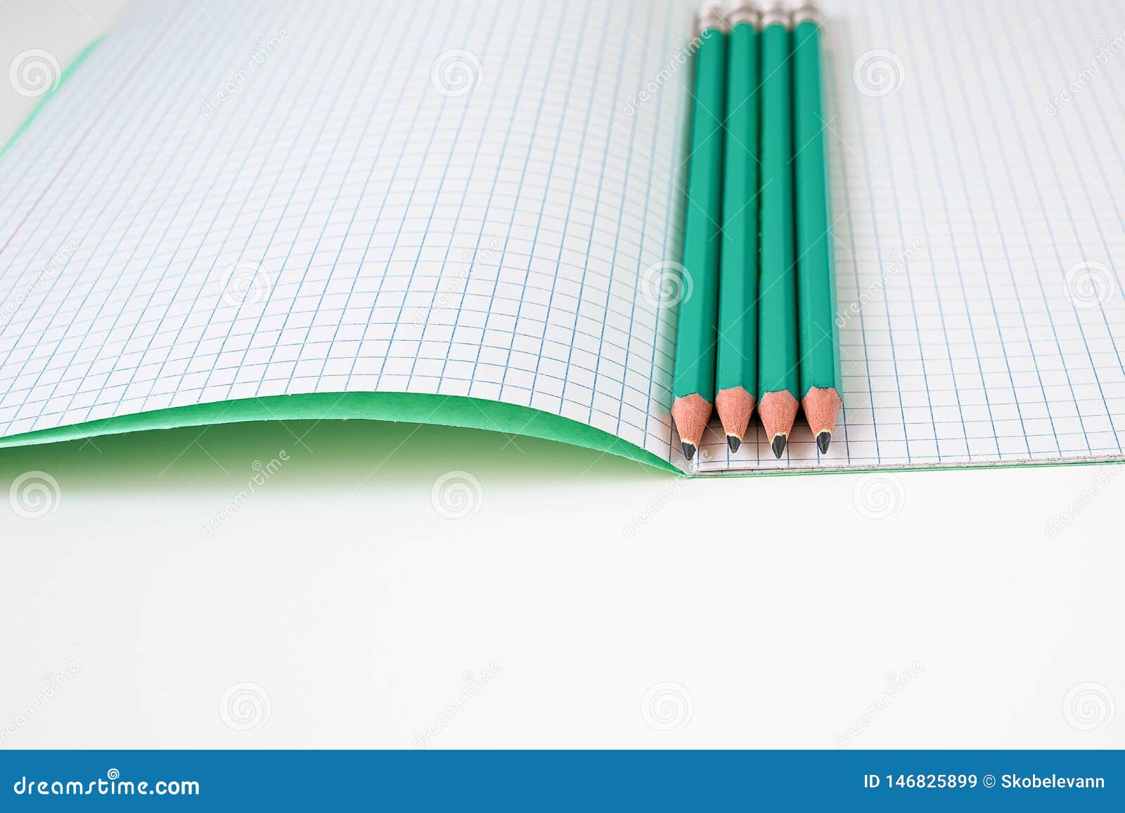 L?pis ao lado do caderno da escola. Green pencils with his hands lie on a white table. Three pencils lie nicely next to notebooks in a cage. Notebooks and pencils are ready for class.