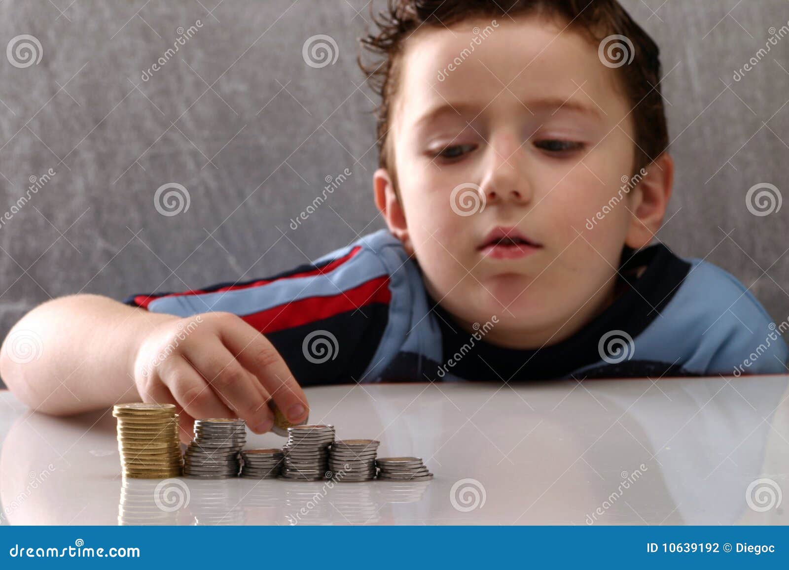 L'épargne. Petit garçon comptant et empilant l'argent, pièces de monnaie.