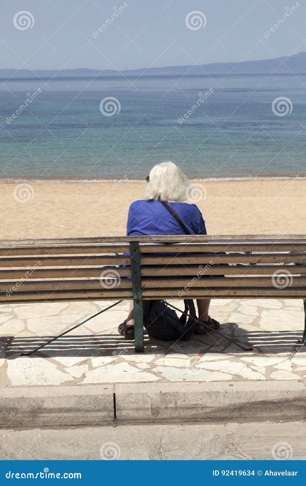 La dame pluse âgé seul s'assied sur le banc et regarde la mer en Grèce. La dame pluse âgé seul s'assied sur le banc de plage et regarde la mer dans la ville grecque du stoupa