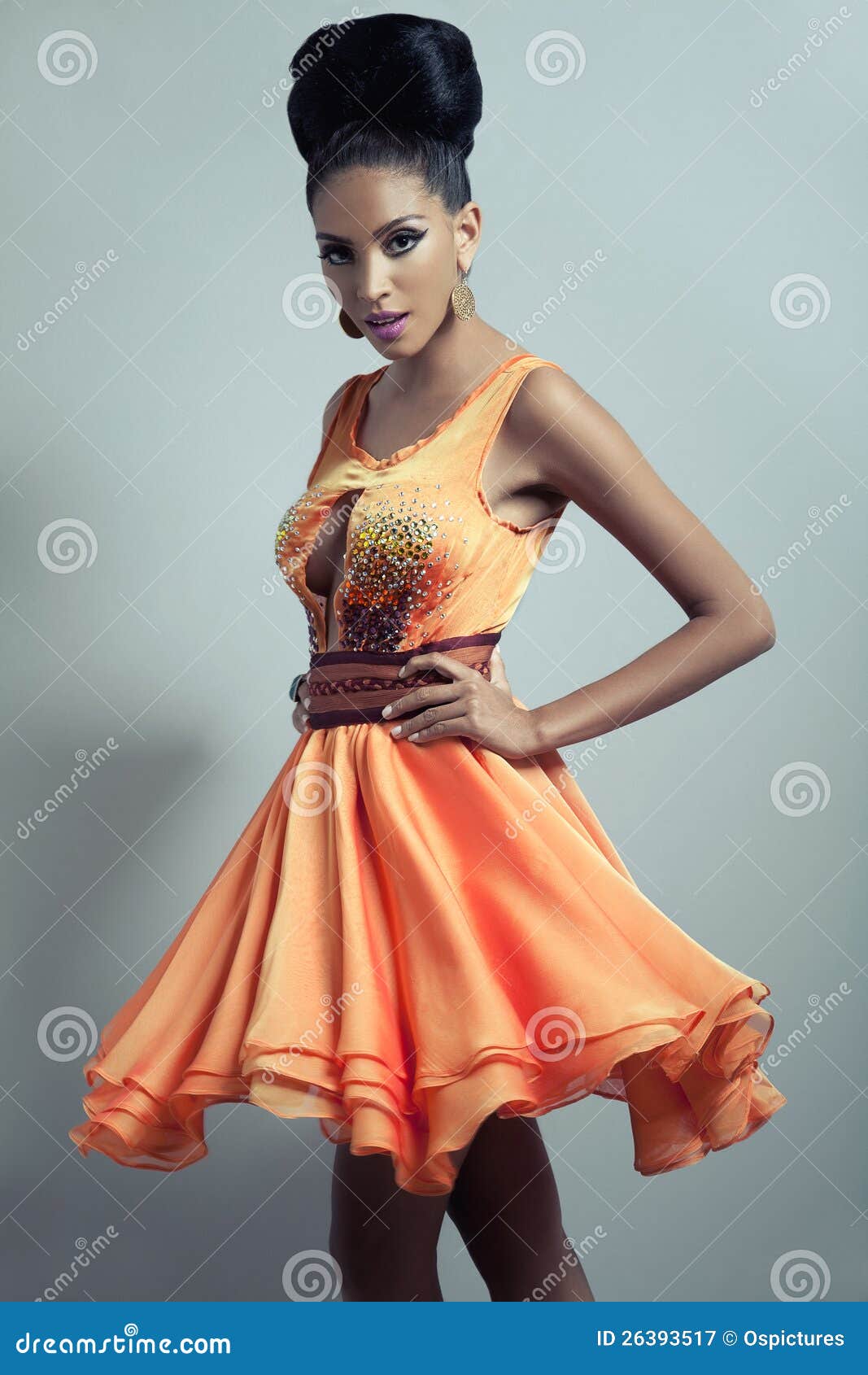 La donna in arancio si è svasata vestito. Modello di modo elegante e affascinante che mostrano fuori ad un progettista vestito arancione con la parte superiore di pizzo, pannello esterno centrale e svasato decorato fatto con parecchi strati di materiale.