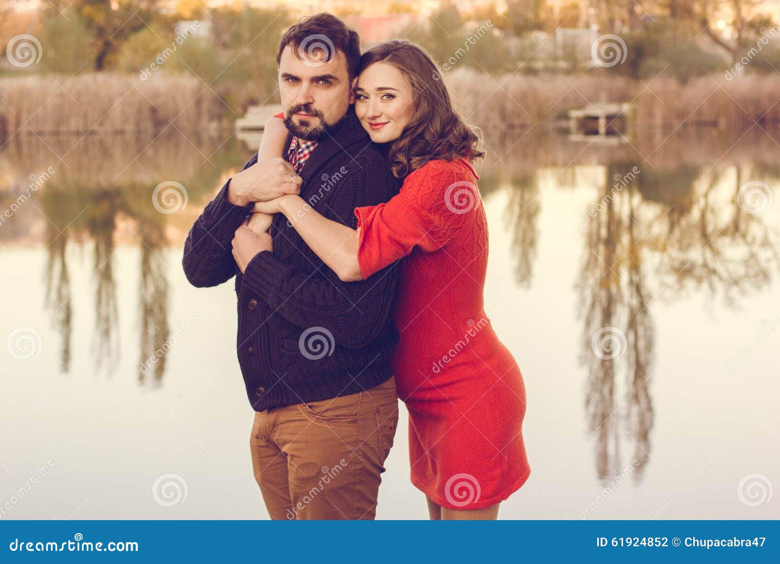 La donna e l'uomo felici delle coppie stanno riposando vicino al lago. I genitori felici moglie e marito di futuro stanno indossando i vestiti caldi che spendono il tempo nel parco di autunno vicino al grande lago