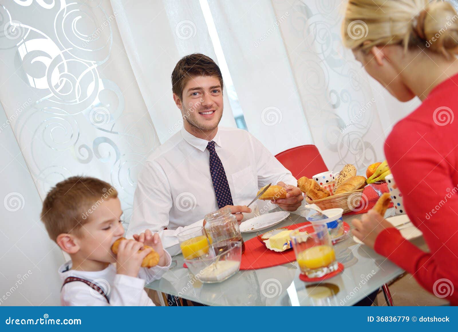 La famille prennent le petit déjeuner sain à la maison. La jeune famille heureuse prennent le petit déjeuner sain à la cuisine avec les détails rouges sur la lumière lumineuse de matin