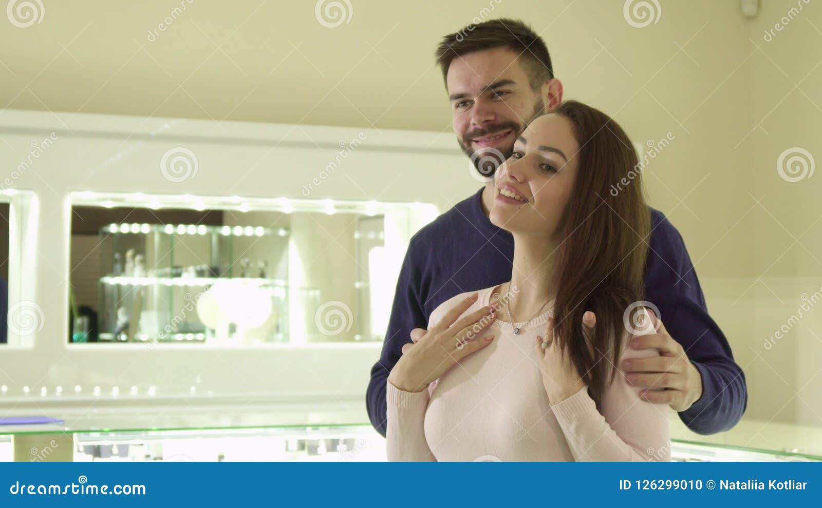 La fille essaye le collier à la boutique de bijoux. Fille assez caucasienne essayant sur le neckclace à la boutique de bijoux Les hommes barbus beaux mettant ses mains sur son ` s d'amie épaule Type attirant de brune attachant le collier derrière le cou du ` s de femme