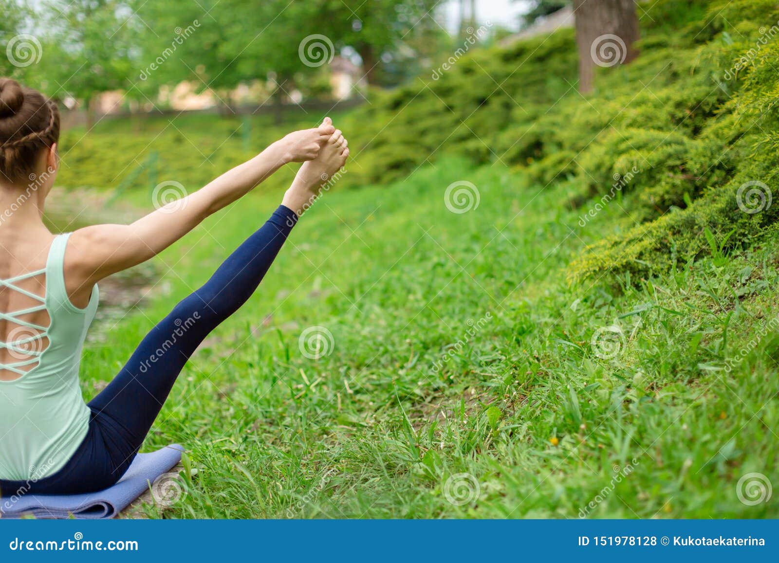 La giovane yoga castana snella si esercita stimolanti di yoga su erba verde contro un fondo della natura