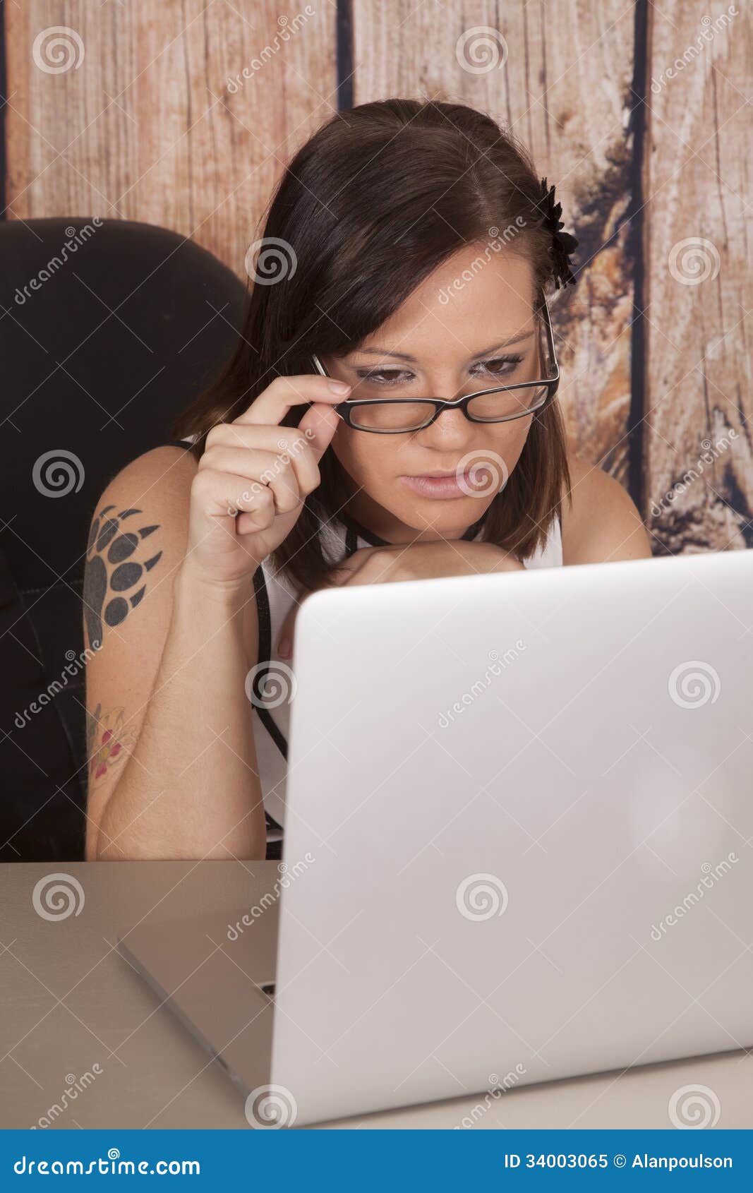 La madera blanca del ordenador del vestido de la mujer sienta el tatuaje de la garra. Una mujer que trabaja en su ordenador que estudia mirando su ordenador
