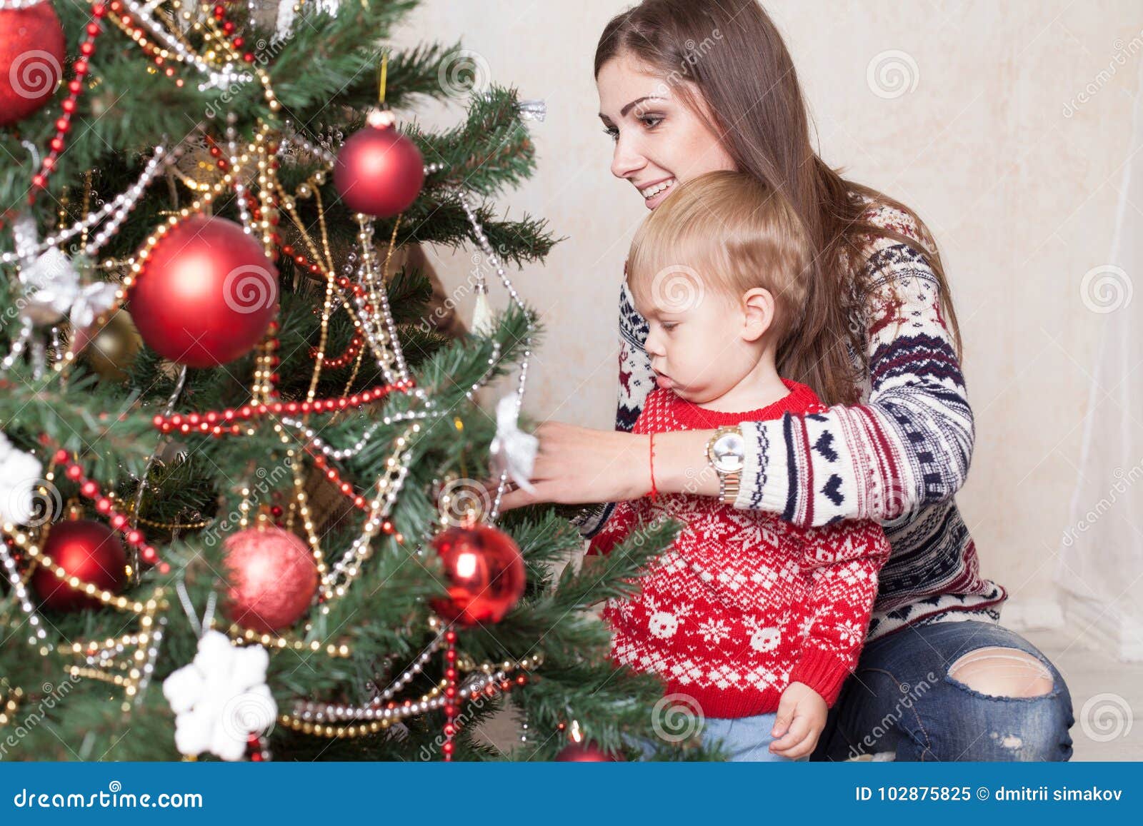 La mamá con el hijo adorna el árbol en la Navidad de los regalos del ` s del Año Nuevo. La mamá con el hijo adorna el árbol de navidad en la Navidad de los regalos del día del ` s del Año Nuevo