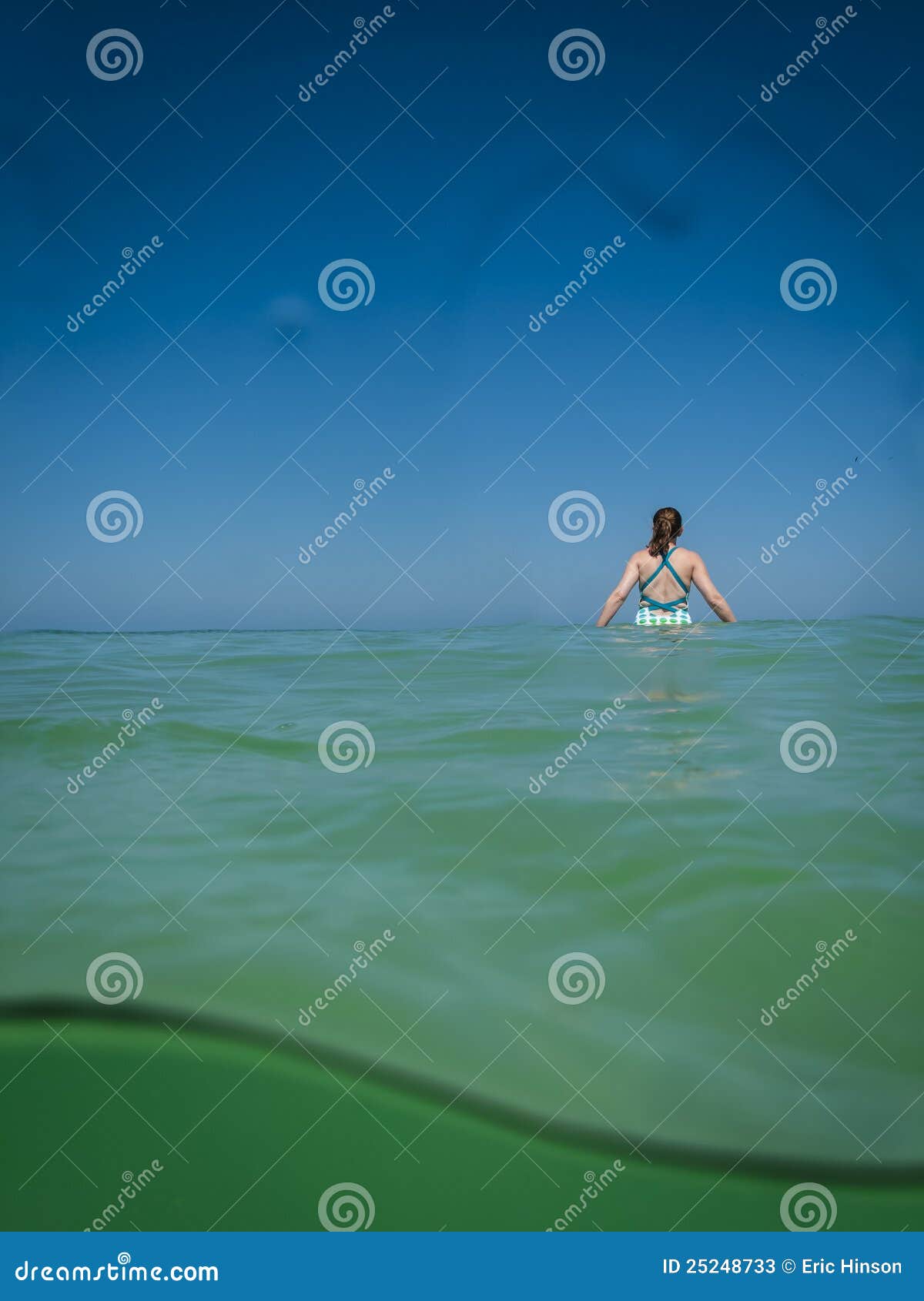 La marche dans l'eau dans le Golfe arrose. Une jeune femme dans un maillot de bain marche dans l'eau dans les eaux calmes et chaudes de côte de Golfe sous les cieux bleus propres et clairs.