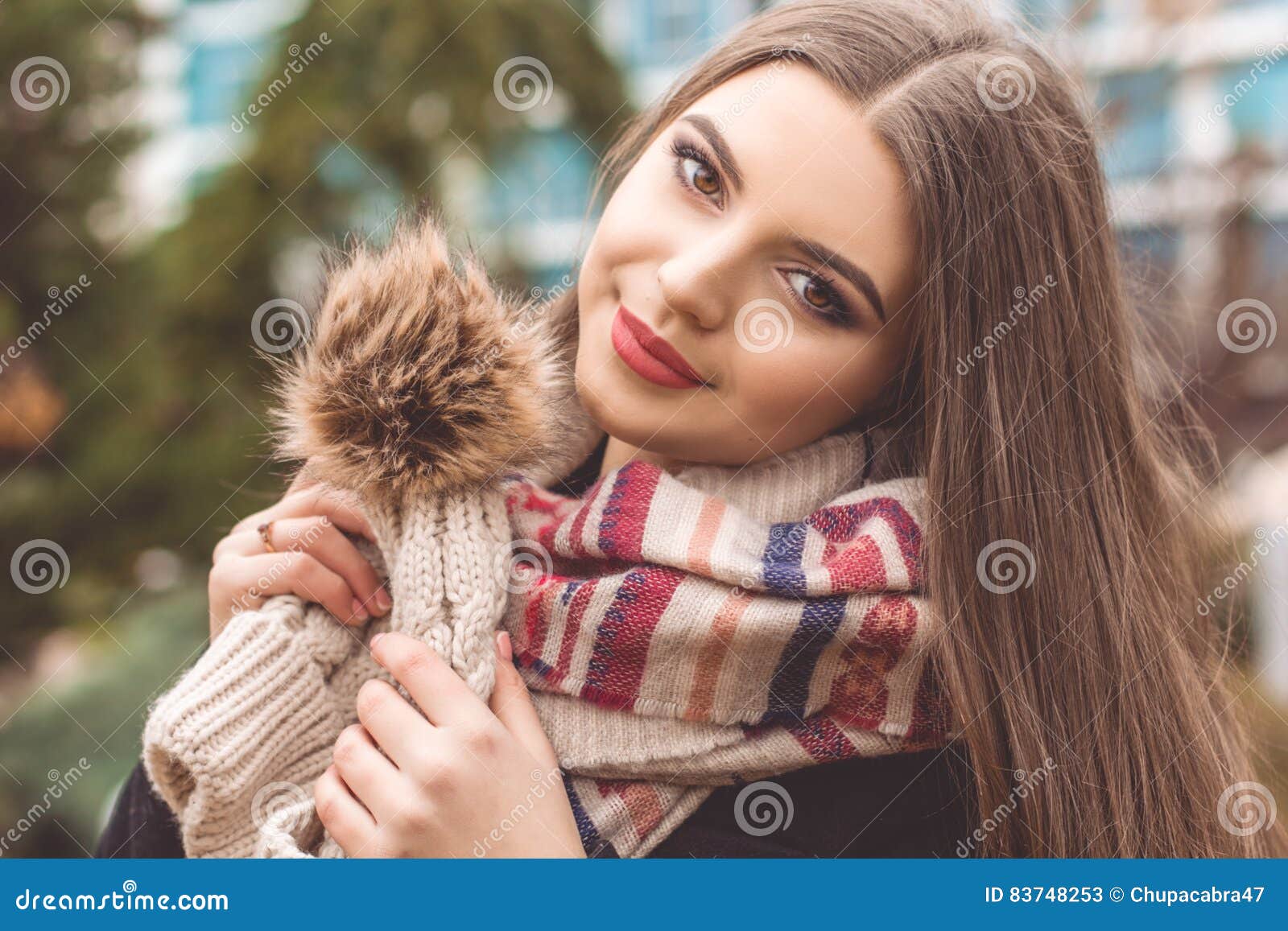 La muchacha bastante adolescente está llevando la ropa caliente del invierno. El retrato del primer de la muchacha sonriente hermosa del adolescente con la piel perfecta está llevando el sombrero caliente y la bufanda del invierno que presentan al aire libre Concepto de la moda de la caída y del invierno