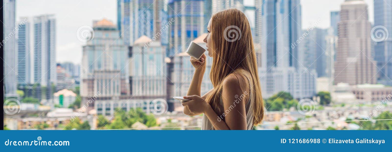 La mujer joven bebe el café por la mañana en el balcón que pasa por alto la ciudad grande y el formato largo de la BANDERA de los. La mujer joven bebe el café por la mañana en el balcón que pasa por alto la ciudad y los rascacielos grandes formato largo de la bandera