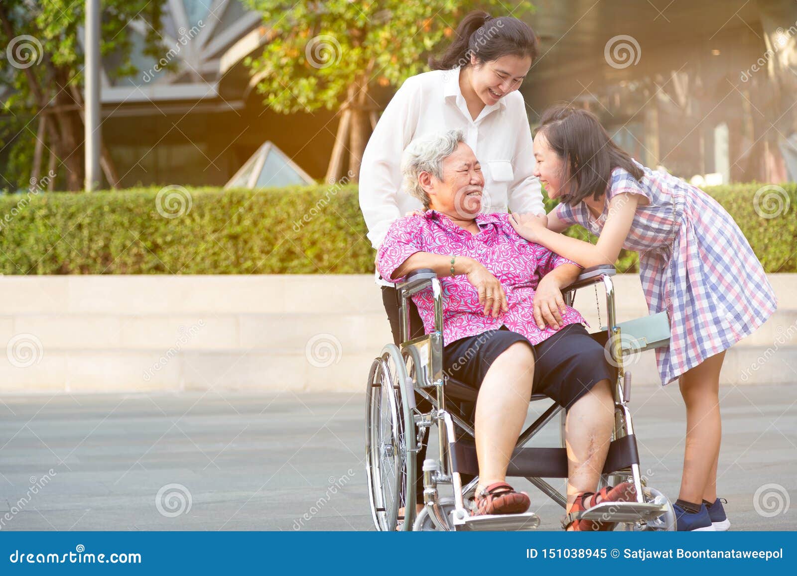 La mujer mayor asiática que tiene felicidad y que sonríe con su hija y nieta en la silla de ruedas en el parque al aire libre, mu. Las mujeres mayores asiáticas que tienen felicidad y que sonríen con su hija y nieta en la silla de ruedas en el parque al aire libre, las mujeres mayores son felices con su familia, muchacha del niño que tiene charla de la diversión, riendo juntas, concepto de familia feliz